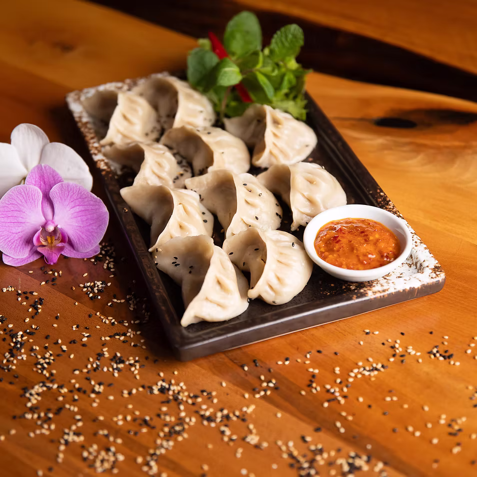 Frisch zubereitete Momos auf einem Tablett mit Dip und Blumen auf einem Holztisch, Sushi Momo Palace Luzern