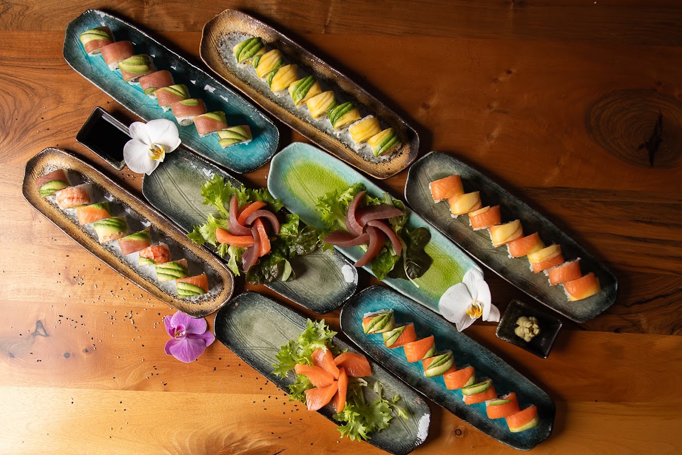 Überblick über mehrere lange Keramikplatten mit frischem Sushi auf einem Holztisch bei Sushi Momo Palace